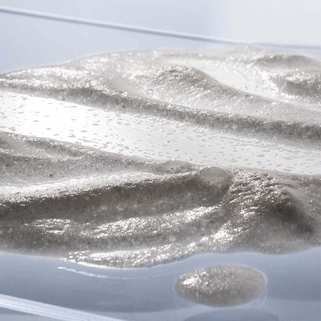 Nahaufnahme eines glitzernden, halbtransparenten Gels mit strukturierter Oberfläche und Bläschen, das an Daily Microfoliant | Gesichtspeeling erinnert.